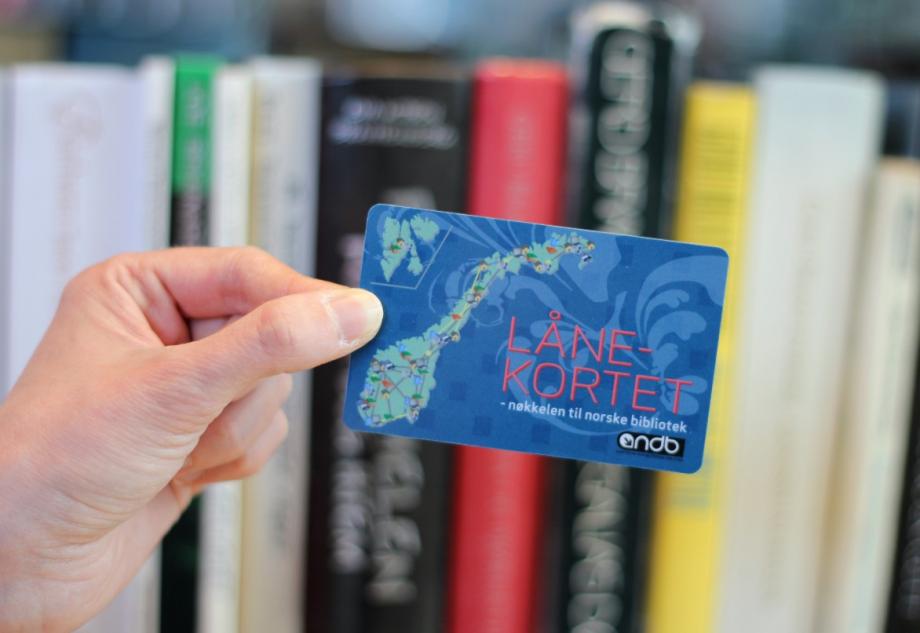 En hånd holder et blått kort med en illustrasjon av Norge og Svalbard i grønt. På kortet står det "Lånekortet - nøkkelen til norske bibliotek". Foto.