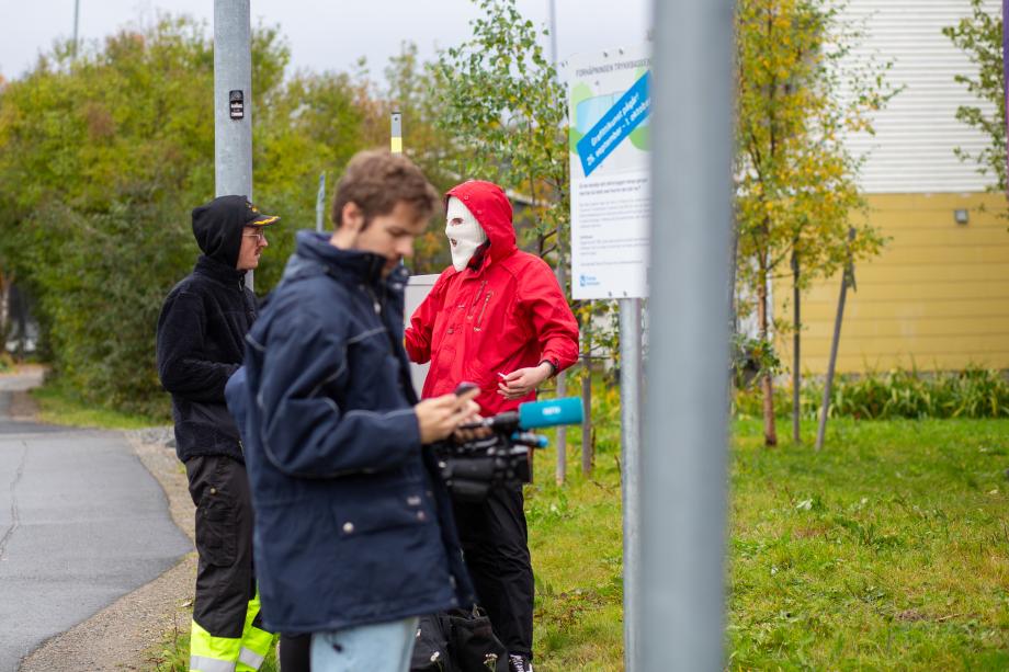 NRK-journalist filmer mens to gatekunstnere står og venter.