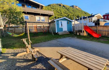Dalen familiebarnehage uteområde med lekehus, husker, benker og bord en solrik sommerdag med blå himmel