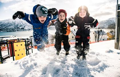 Tre glde barn hopper i snøen i Gyllenvang barnehage 