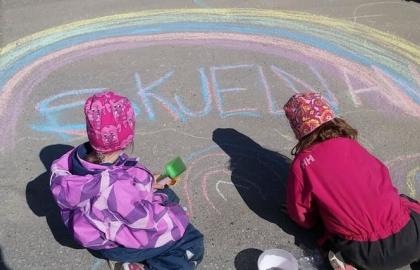 To barn tegner regnbue med kritt i barnehagens uteområde en solrik sommerdag