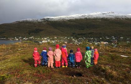 Ti barnehagebarn som står på en topp på tur en tidlig høstdag