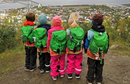 Fem barnehagebarn med grønne ryggsekker på fjelltur med utsikt over Tromsøya en sommerdag 