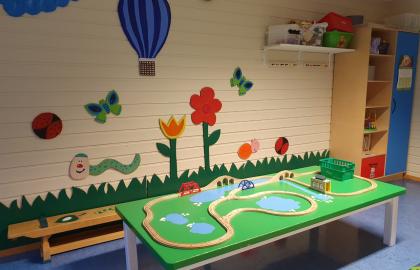 Lekeområde med malte blomster og luftballong på veggen og et grønt bord med togskinner i tre