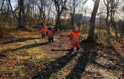 Tre barn med refleksvester på tu i skogen ved Norlandia friluftsbarnehage